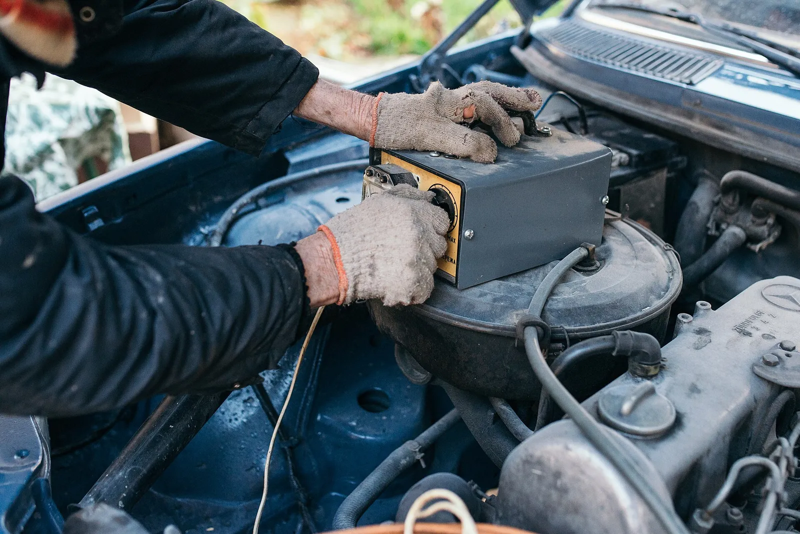 Mecánico con guantes midiendo la carga de una batería de auto (foto ilustrativa)
